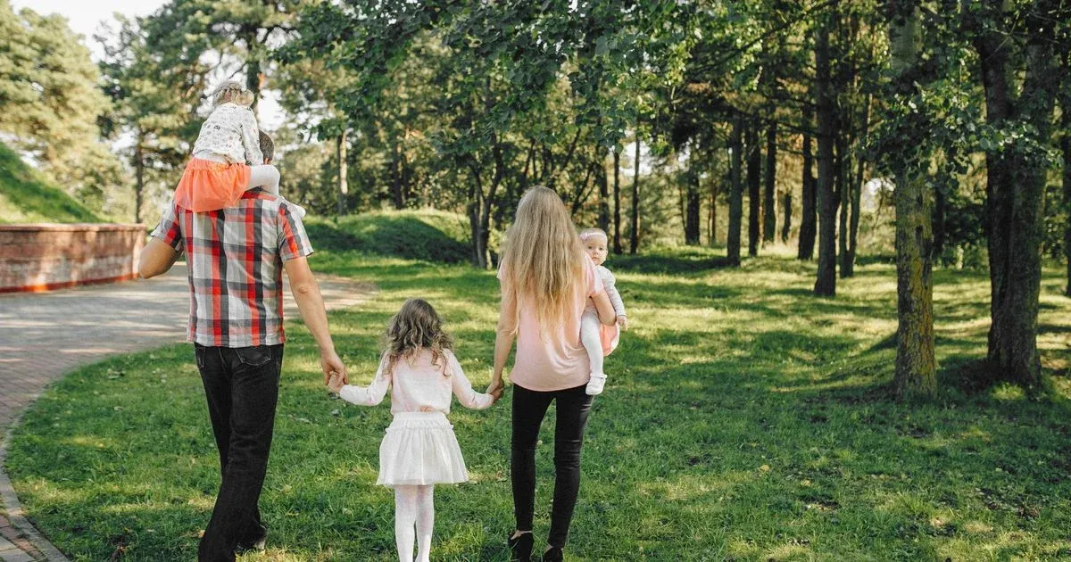A family with two young children walking along a path in a park