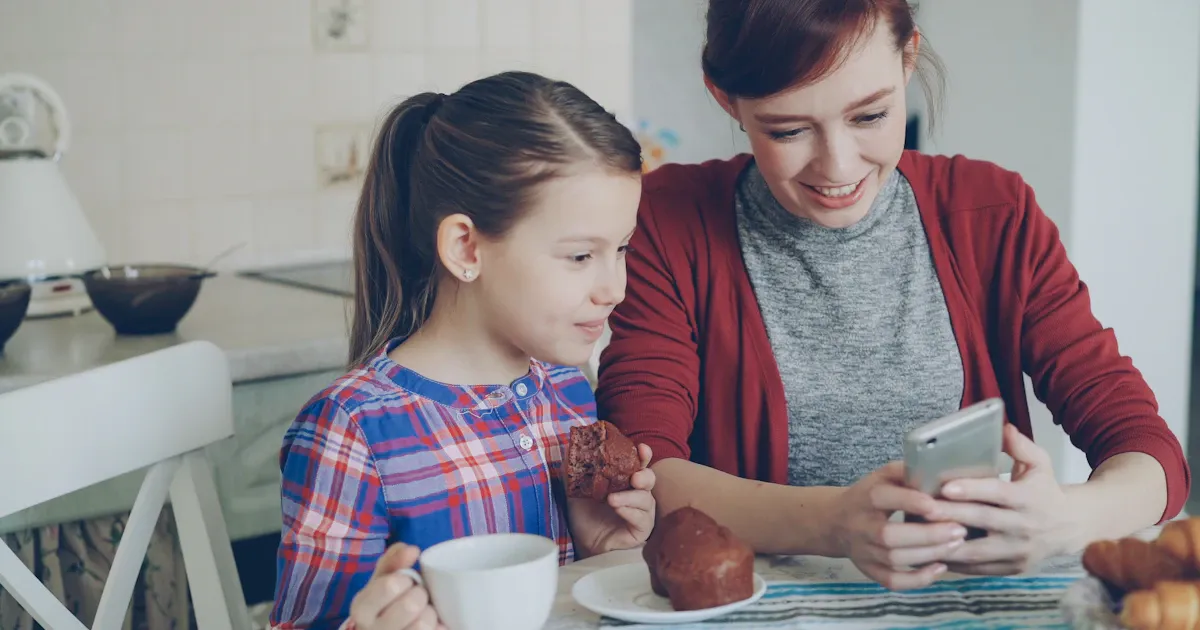 Une mère et sa fille regardent ensemble un smartphone à la table de la cuisine