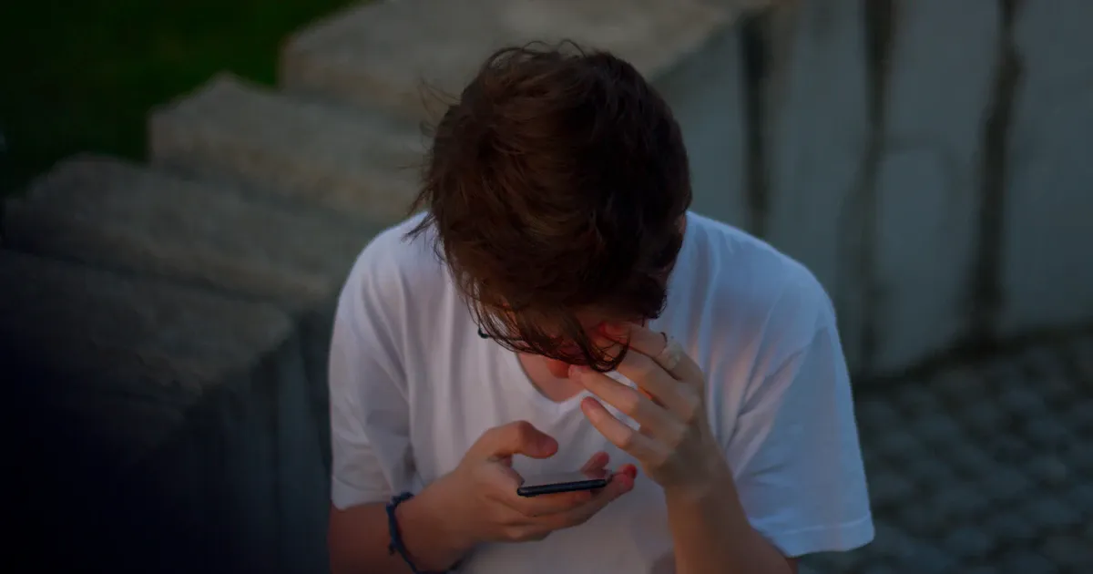 Un ragazzo guarda lo smartphone con la mano sulla fronte, preoccupato