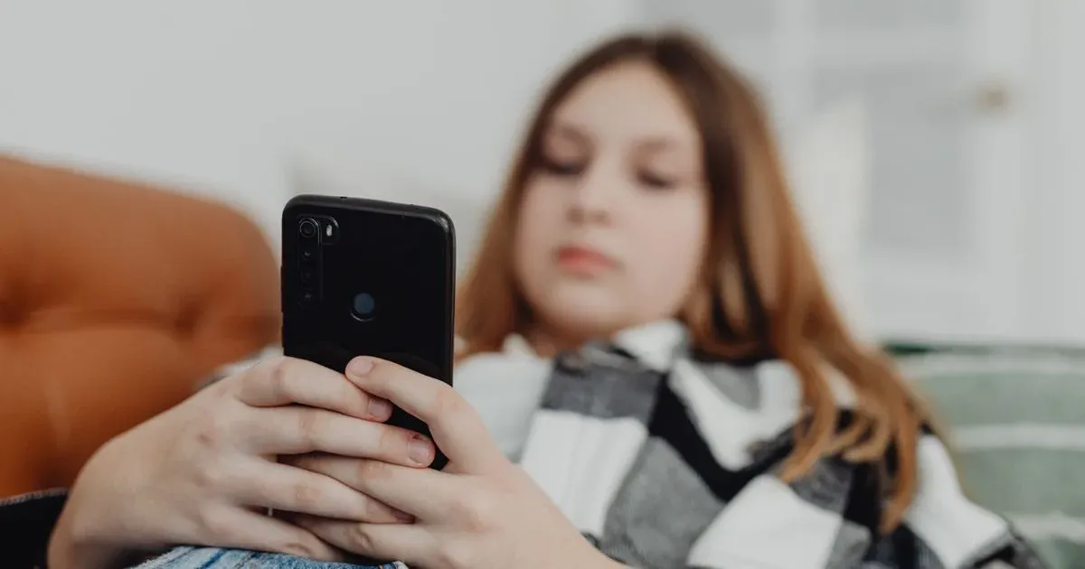 Kanepede uzanmış genç bir kız akıllı telefonunu kullanıyor