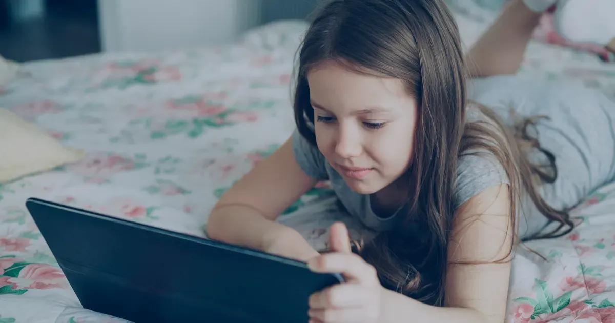 Une fillette allongée sur son lit utilise une tablette