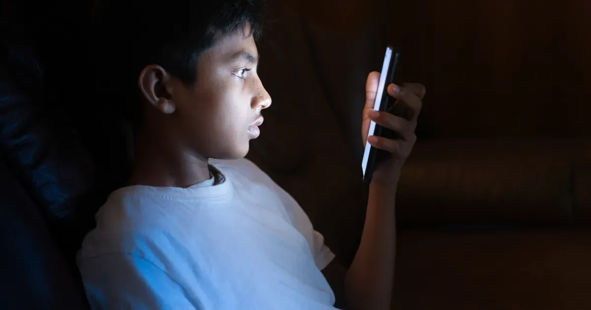 Ein Junge schaut in einem dunklen Zimmer auf sein Smartphone