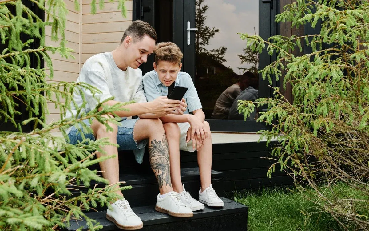 Vader en zoon zitten op een trapje en kijken samen naar een smartphone